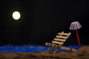 A bench with an umbrella putting on the timber that have blue sea and moon as the background photo