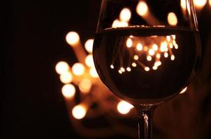 A glass of wine has the shadow of yellow and orange bokeh light on it which isolated on dark color background photo