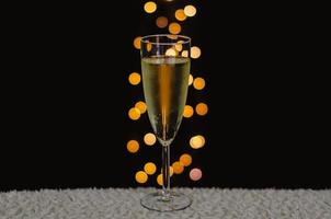 A glass of sparkling wine with bokeh lights on dark background. photo