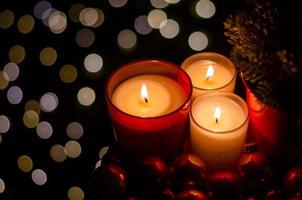 Selective focus on burning candle in red glass with Christmas tree decorated with bauble ornaments with bokeh light in dark background. photo