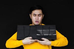 Asian male acting amaze and holding shopping bags on dark background for Black Friday concept. photo