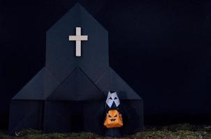 The Halloween background of origami or Paper folding about the nun holding pumpkin head jack-o-lantern in front of black church with messy lawn photo