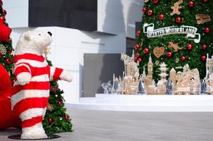 Teddy bear wears red dress standing beside Christmas tree for Christmas holiday decoration. photo