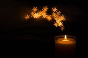 Aromatic candle with flame and snowflake shape bokeh on dark background for Thanks giving and Christmas day. photo