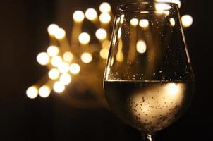 A glass of wine has the shadow of yellow and orange bokeh light on it which isolated on dark color background photo