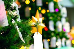 Paper hanging on Christmas tree for Holiday decoration with colorful lights on background. photo