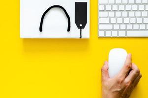 mano que sostiene el mouse inalámbrico con teclado para compras en línea sobre fondo amarillo. concepto de lunes cibernético y viernes negro. foto