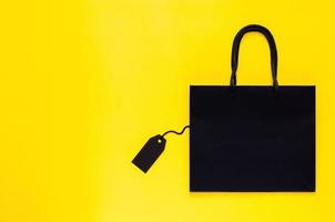 Black shopping paper bag with blank black price tag on yellow background for Black Friday shopping sale concept. photo