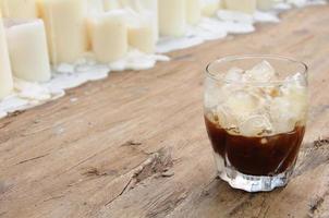 un vaso de espresso agitado sobre una mesa de madera decorada con velas que mezclan cubitos de hielo con café para una bebida fría para disfrutar del clima cálido del verano. foto