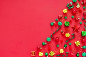 Christmas tree made of New year ornament decorations on red background. Flat lay minimal Holiday concept. photo