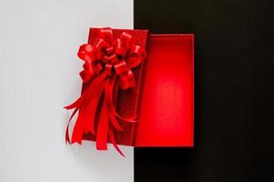 Red christmas box with red bow ribbon on black and white background. Black Friday concept. photo