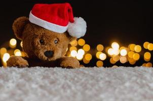 Brown teddy bear wearing santa claus hat with Christmas lights background. photo