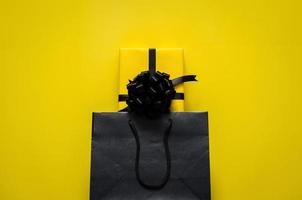 A yellow gift box puts in black shopping bag with yellow background. Black friday and Boxing day concept. photo