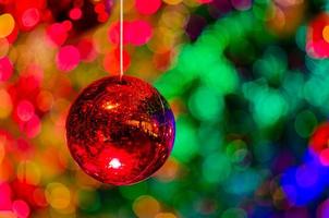 adorno rojo colgando para decorar para las vacaciones de navidad con un colorido bokeh de luz y otros adornos. foto