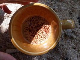una taza de café con leche en un vaso marrón sobre un fondo de arena de playa foto