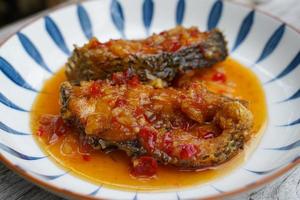 Fried fish with chilli in a ceramic plate on an old wooden floor. The taste is sour, sweet and slightly spicy. photo