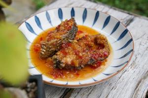 pescado frito con chile en un plato de cerámica sobre un suelo de madera antiguo. el sabor es agrio, dulce y ligeramente picante. foto