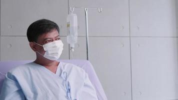 ett äldre manlig patient tar av en mask och sitter på de patientens säng. asiatisk man är inlagd på sjukhus med covid19. video