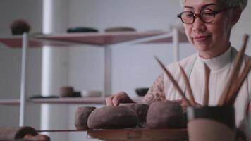Aziatisch ouderen vrouw genieten van pottenbakkerij werk Bij huis. een vrouw keramist is maken nieuw pottenbakkerij in een studio video