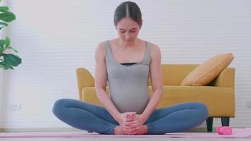 Beautiful young Asian pregnant woman in sportswear is doing yoga at home. video