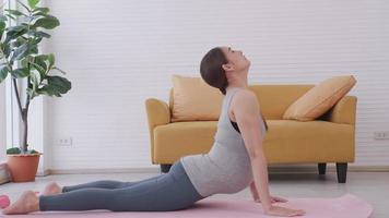 hermosa joven asiática embarazada en ropa deportiva está haciendo yoga en casa.