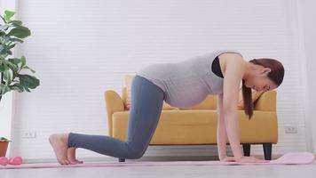 hermosa joven asiática embarazada en ropa deportiva está haciendo yoga en casa. video