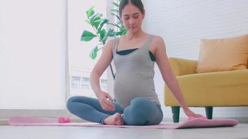 hermosa joven asiática embarazada en ropa deportiva está haciendo yoga en casa. video