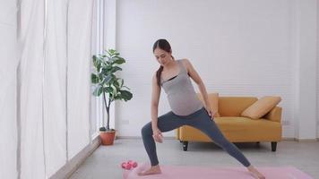 Beautiful young Asian pregnant woman in sportswear is doing yoga at home. video