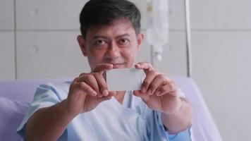 älterer asiatischer männlicher patient, der während des krankenhausaufenthalts eine lebensversicherungskarte hält. video