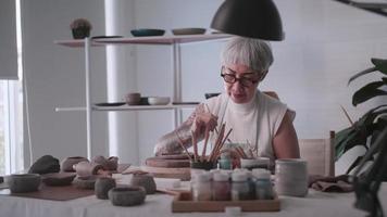 Aziatisch ouderen vrouw genieten van pottenbakkerij werk Bij huis. een vrouw keramist is maken nieuw pottenbakkerij in een studio video