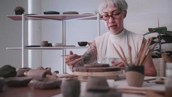 Asian elderly woman enjoying pottery work at home. A female ceramicist is making new pottery in a studio