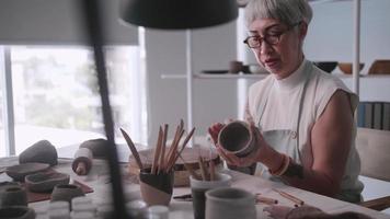 asiatisk äldre kvinna njuter krukmakeri arbete på Hem. en kvinna keramiker är framställning ny krukmakeri i en studio