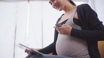 mujer embarazada asiática que usa una tableta para consultar en línea con un obstetra video