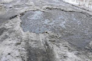 Damaged asphalt road with potholes caused by freezing and thawing cycles during the winter. Poor road photo