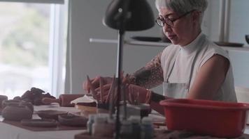 Asian elderly woman enjoying pottery work at home. A female ceramicist is making new pottery in a studio video