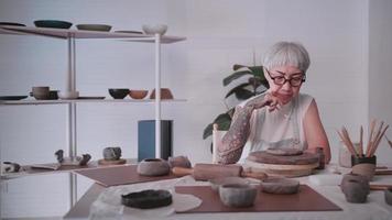 mulher idosa asiática desfrutando do trabalho de cerâmica em casa. uma ceramista feminina está fazendo nova cerâmica em um estúdio video
