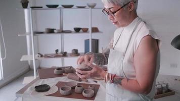 asiatico anziano donna godendo ceramica opera a casa. un' femmina ceramista è fabbricazione nuovo ceramica nel un' studio video