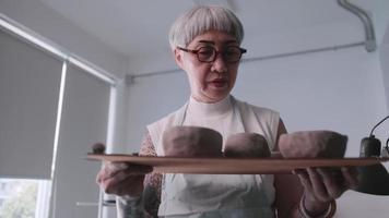 asiatisk äldre kvinna njuter krukmakeri arbete på Hem. en kvinna keramiker är framställning ny krukmakeri i en studio video