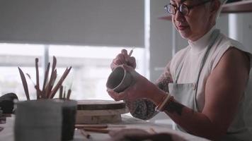 femme âgée asiatique appréciant le travail de poterie à la maison. une céramiste féminine fabrique de nouvelles poteries dans un studio video