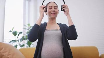 mujer embarazada asiática feliz poniendo auriculares en su vientre. video