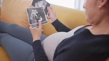 femme enceinte asiatique heureuse regardant l'image échographique sur le canapé. video
