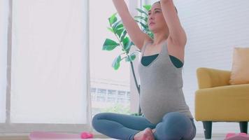 hermosa joven asiática embarazada en ropa deportiva está haciendo yoga en casa. video