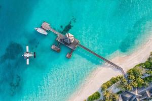 Beautiful aerial view of Maldives shore, jetty villa seaplane top view, wooden boat Dhoni and tropical beach. Palm trees white sand, sea. Luxury travel and vacation concept. Amazing aerial landscape photo