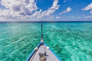 barco en aguas turquesas del océano contra el cielo azul con nubes blancas sobre la laguna tropical. paisaje marino natural para vacaciones de verano, vista panorámica en las islas maldivas. barco dhoni, viaje exótico foto