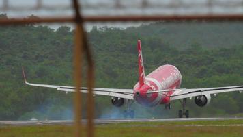 phuket, tailandia 26 de noviembre de 2017 - aerolínea de bajo costo de airasia aterrizando, tocando la pista y frenando en el aeropuerto de phuket. vista de la tira a través de la valla. concepto de turismo y viajes video