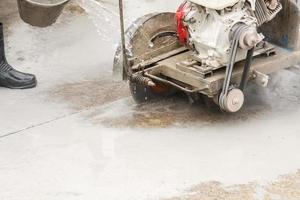 Worker using diamond saw blade machine cutting concrete road at construction site photo