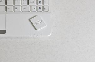 A compact SD memory card lies on a white netbook. The digital information storage device is ready for use. Concept of modern technologies photo