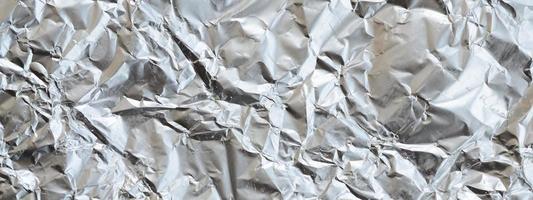 Thin wrinkled sheet of crushed tin aluminum silver foil background with shiny crumpled surface for texture photo