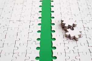 The green path is laid on the platform of a white folded jigsaw puzzle. The missing elements of the puzzle are stacked nearby. Texture image with space for text photo