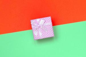 Small pink gift box lie on texture background of fashion pastel turquoise and red colors paper photo